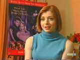 Alyson Hannigan en pull bleu sans manche devant une affiche de Buffy